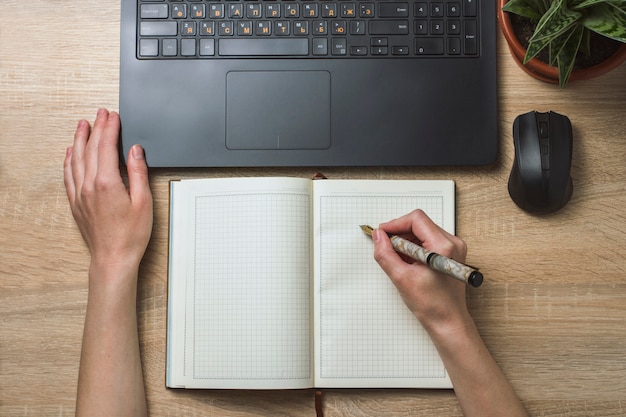 Manos femeninas cuaderno diario y ratón inalámbrico. Espacio de oficina y ambiente de trabajo. Vista superior