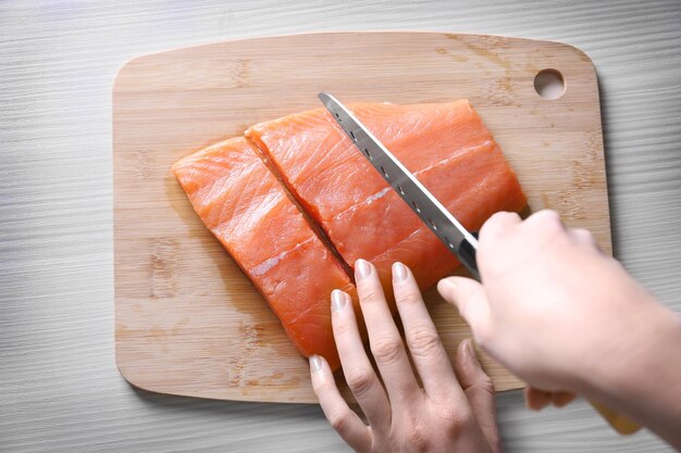 Manos femeninas con cuchillo cortando filete de salmón fresco en tablero de madera