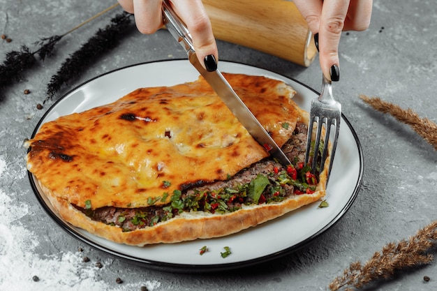 Manos femeninas con un cuchillo y un tenedor cortan Khachapuri con cordero y chile. Comida nacional georgiana.