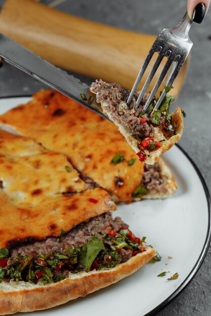 Manos femeninas con cuchillo y tenedor cortan Khachapuri con cordero y chile. Comida nacional georgiana.