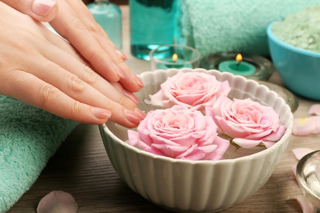 Foto manos femeninas y cuenco de agua de spa con flores de cerca