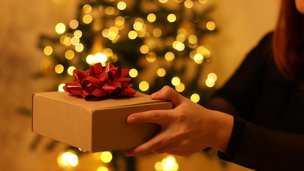 Manos femeninas dan caja de regalo sorpresa en el fondo de la decoración del árbol de Navidad. Navidad, año nuevo, concepto de cumpleaños.