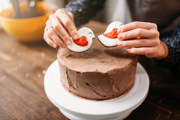 Manos femeninas decoran pastel con galletas en forma de pájaros. Cocina casera de postre sabroso