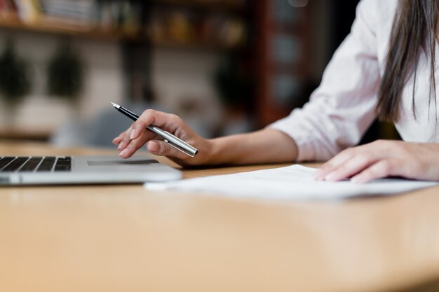 Manos femeninas desplazándose en la computadora portátil y tomando notas con lápiz