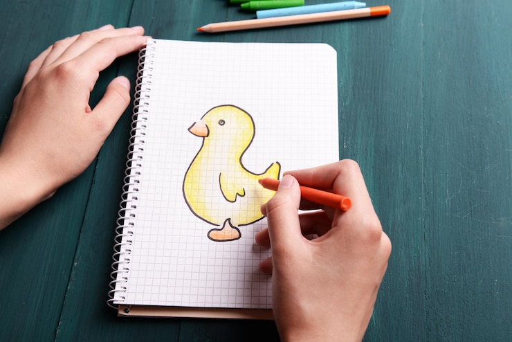 Foto manos femeninas dibujando pato en cuaderno sobre fondo de mesa de madera