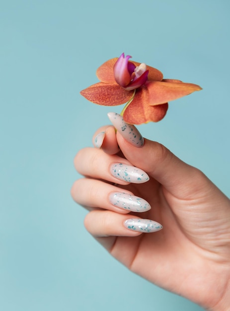 Manos femeninas con diseño de uñas azules sobre un fondo pastel azul