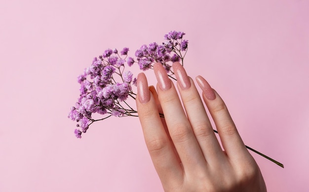 Manos femeninas con diseño de uñas rosadas sostienen flores de gipsófila