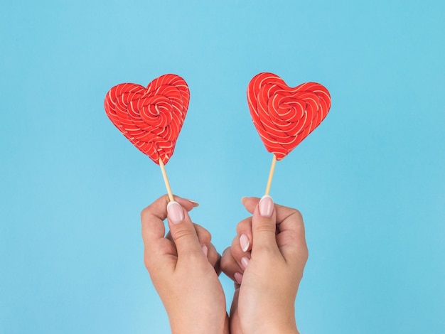 Manos femeninas con dos caramelos en forma de corazón sobre un fondo azul.