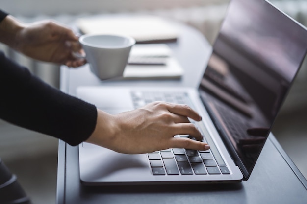 Manos femeninas en un enfoque nítido escribiendo en un entorno de oficina de teclado portátil moderno en un desenfoque suave detrás