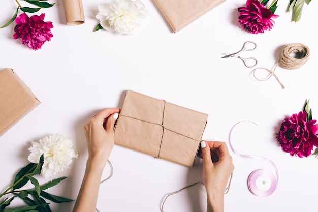 Manos femeninas envolviendo regalos en mesa blanca