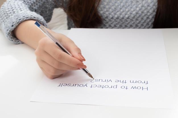 Las manos femeninas escriben en una hoja de papel cómo protegerse del virus