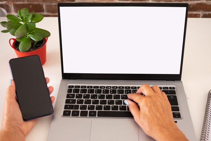 Foto manos femeninas escribiendo en la computadora portátil mientras usa el teléfono móvil. escritorio blanco