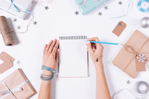 Manos femeninas escribiendo en un cuaderno entre decoraciones navideñas