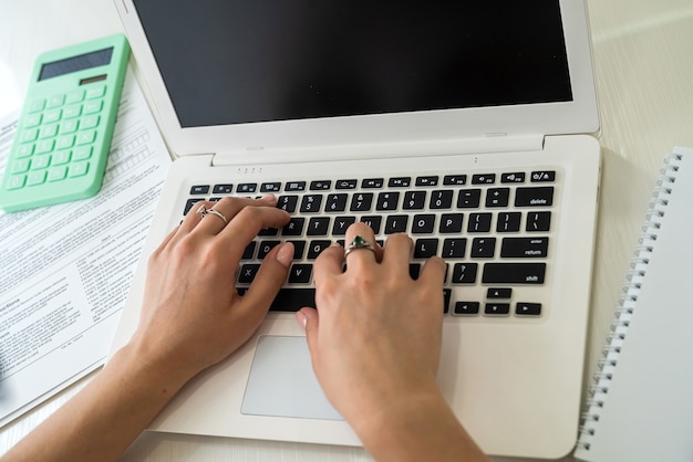 Manos femeninas escribiendo en el teclado de la computadora portátil de cerca.