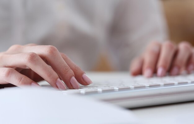 Manos femeninas escribiendo en teclado plateado usando