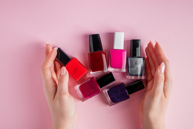 Manos femeninas con esmaltes de uñas brillantes. Un grupo de esmalte de uñas de color sobre un fondo rosa.