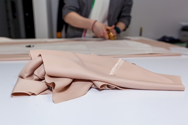 Manos femeninas están cortando la tela con tijeras de sastre en el patrón de papel, sobre una mesa blanca