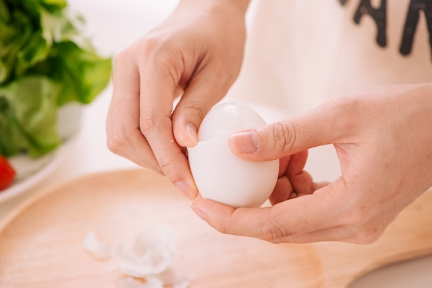 Manos femeninas están desgranando huevos de gallina. La mujer prepara el desayuno en casa. Huevos de gallina cocidos en vajilla de madera sobre una mesa oscura. Tonificación vintage