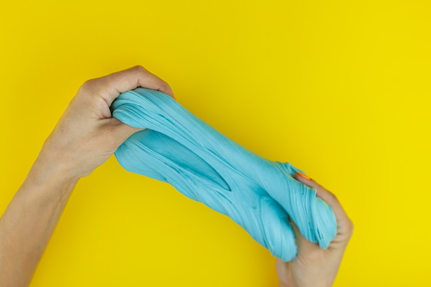 Foto manos femeninas están jugando con limo azul sobre un fondo amarillo. juguete antiestrés. relajación y descanso