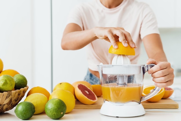 Manos femeninas y exprimidor de cítricos durante la preparación de jugo de naranja fresco