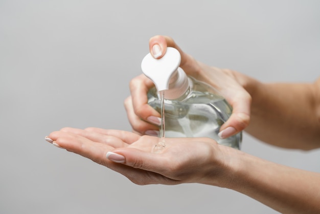 Manos femeninas con gel desinfectante para manos o dispensador de jabón líquido sobre pared gris claro