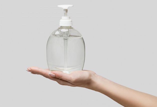 Manos femeninas con gel desinfectante para manos o dispensador de jabón líquido sobre pared gris claro