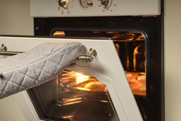 Manos femeninas con guantes abren la puerta del horno
