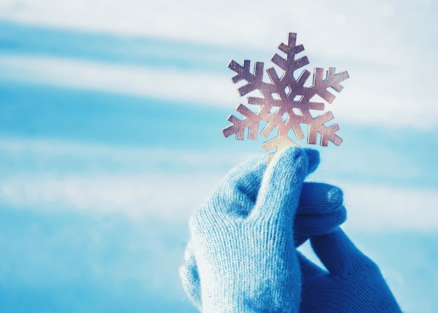 Manos femeninas en guantes azules con un copo de nieve en el fondo de la nieve.