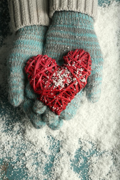 Manos femeninas en guantes con corazón decorativo sobre fondo de nieve