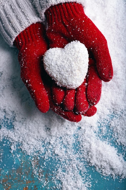Manos femeninas en guantes con corazón decorativo sobre fondo de nieve