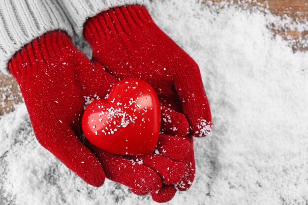 Manos femeninas en guantes con corazón decorativo sobre fondo de nieve