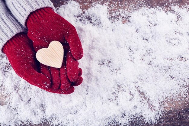 Manos femeninas en guantes con corazón decorativo sobre fondo de nieve