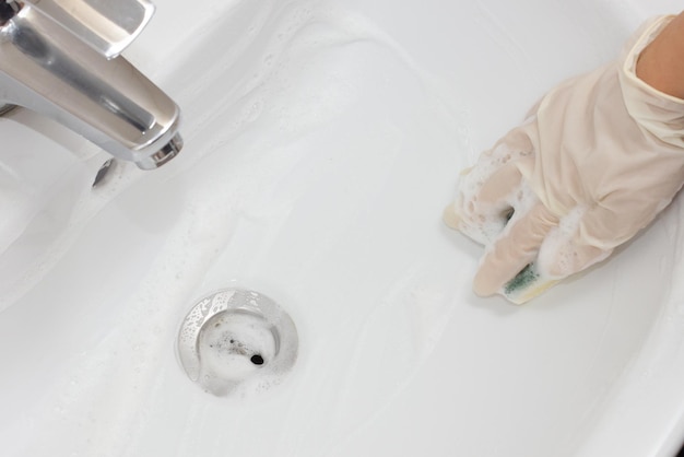 Manos femeninas en guantes lavar un lavabo blanco con una esponja y espuma