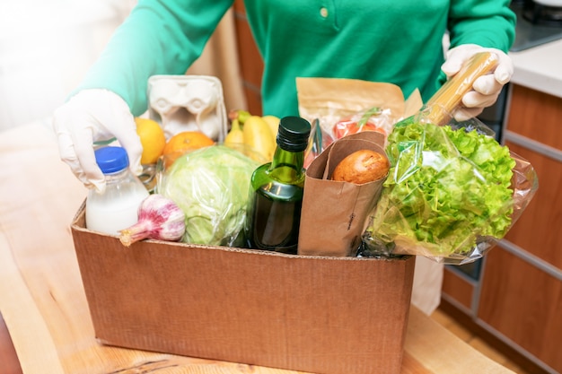 Manos femeninas en guantes protectores sosteniendo una caja con productos alimenticios