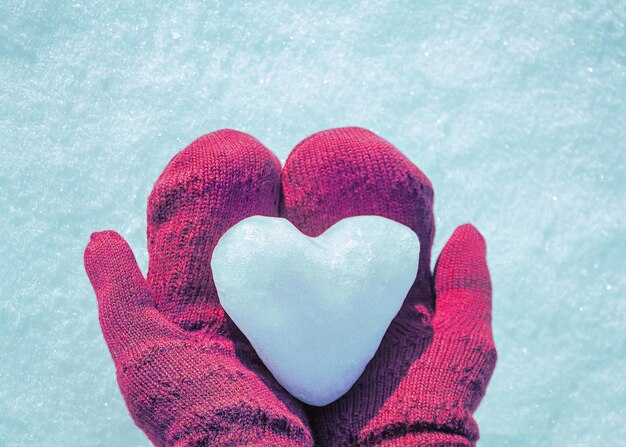 Manos femeninas en guantes tejidos con corazón de nieve en el día de invierno Concepto de amor