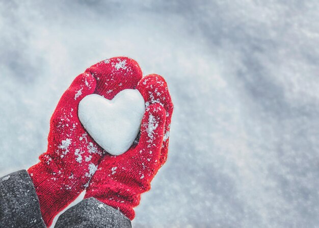 Manos femeninas en guantes tejidos con corazón de nieve en el día de invierno Concepto de amor