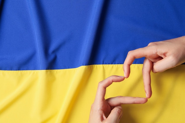 Manos femeninas hacen forma de corazón en el fondo de la bandera ucraniana