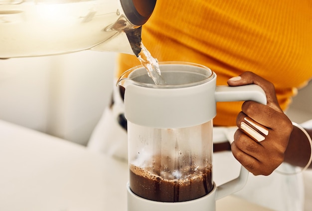 Manos femeninas haciendo café por la mañana para disfrutar con el desayuno vertiendo agua caliente de la tetera en una cocina Primer plano de una mujer negra casual preparando o preparando té o bebida espresso en casa