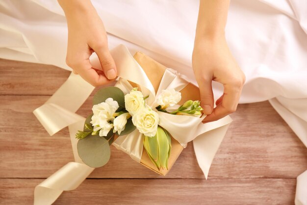Manos femeninas haciendo caja de regalo con flores en la mesa de madera