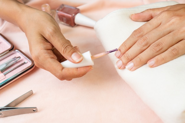 Manos femeninas haciendo esmalte de uñas en color rosa perla con un conjunto de instrumentos de manicura y herramientas en terciopelo de seda rosa. belleza, concepto de manicura