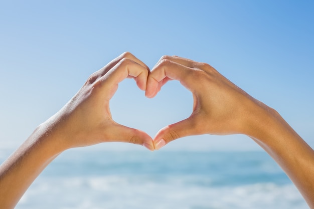 Manos femeninas haciendo forma de corazón junto al mar