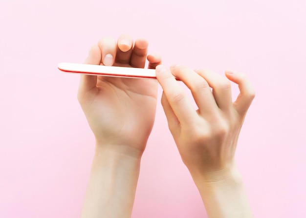 manos femeninas haciendo una manicura sobre un fondo rosa