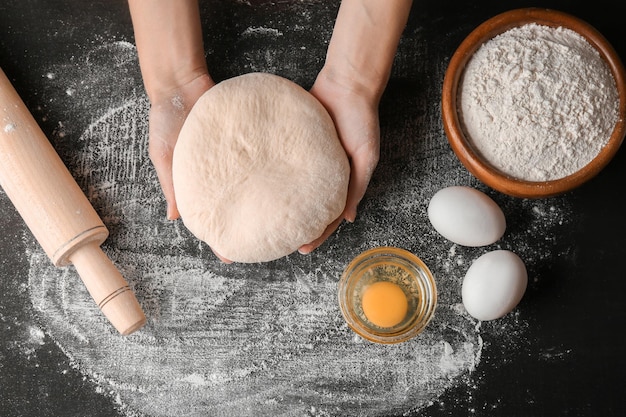 Manos femeninas haciendo masa para pizza en mesa negra