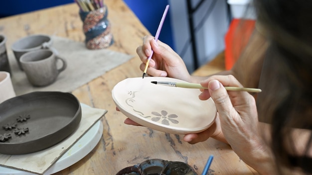Manos femeninas haciendo un plato de cerámica pintando y dibujando en un plato de cerámica