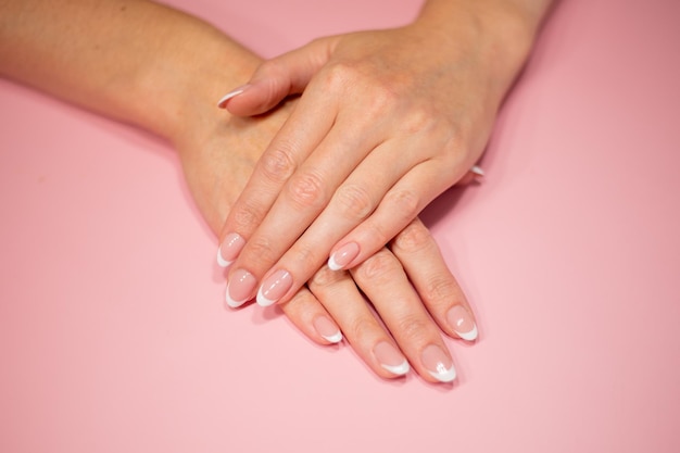 Manos femeninas con hermosa manicura blanca francesa clásica Dedos aislados en un fondo rosa pastel