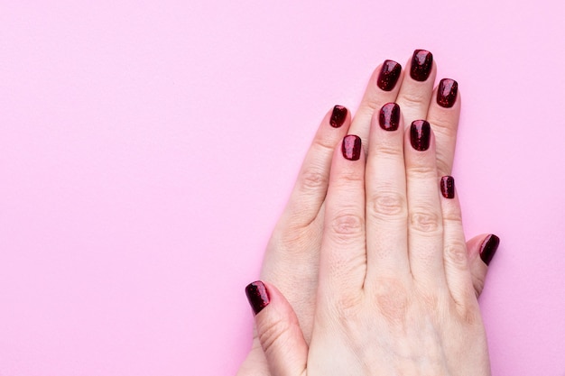 Manos femeninas con hermosa manicura - uñas brillantes de color rojo oscuro en la pared rosa con espacio de copia.