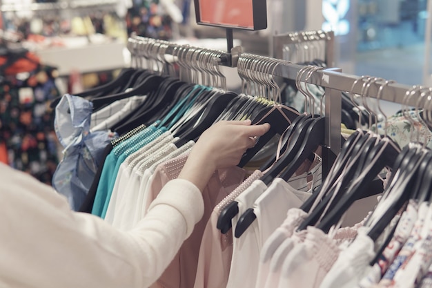 Foto manos femeninas hurgando en ropa en una tienda de segunda mano.