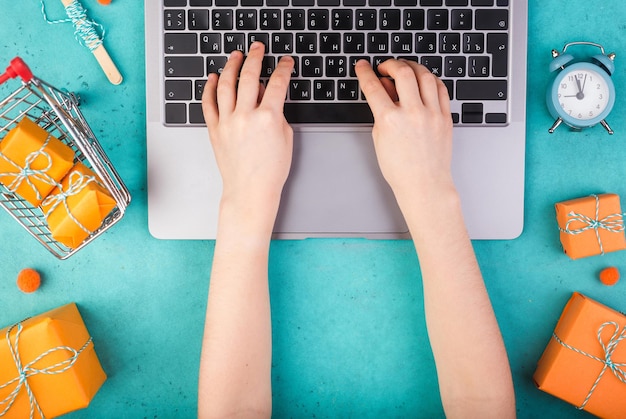 Manos femeninas con laptop y naranja presenta en mesa azul plana concepto de compras en línea de vacaciones ...