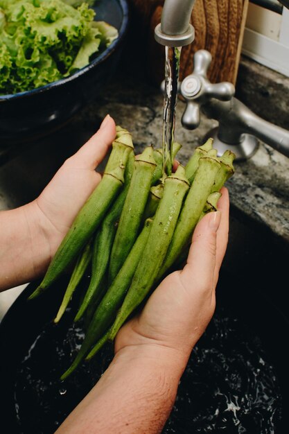 Manos femeninas lavando okra debajo del grifo para cocinar