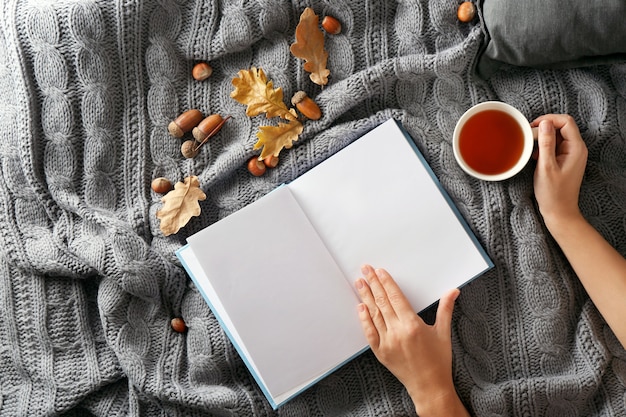 Manos femeninas con libro y taza de té en la cama